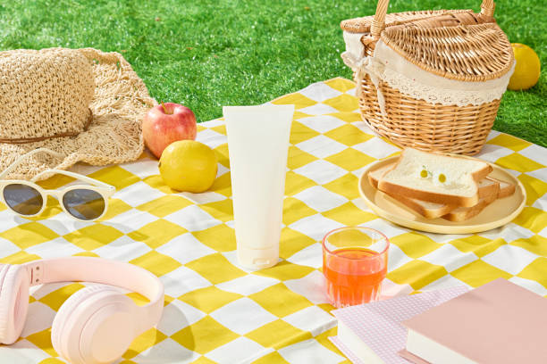 istock Cosmetic mockup for advertising pics from above angle, an empty white tube placed on yellow mat, next to a glass of red liquid, plenty picnic foods and entertainment items displayed around 2157641555