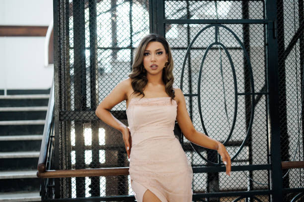 Portrait of beautiful young woman in evening gown standing in front of iron lift in old-fashioned building