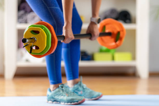 Home fitness routine, a woman performs deadlifts using a barbell bar and weights for strength training.