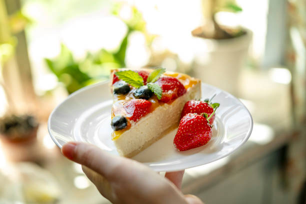 A man's hand holds a plate of appetizing cheesecake with berries. concept of making delicious desserts at home.