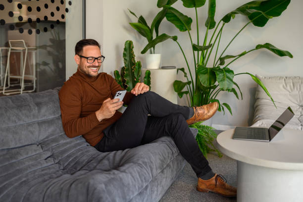 istock Smiling mid adult businessman checking messages over smart phone while sitting on sofa in office 2157651091