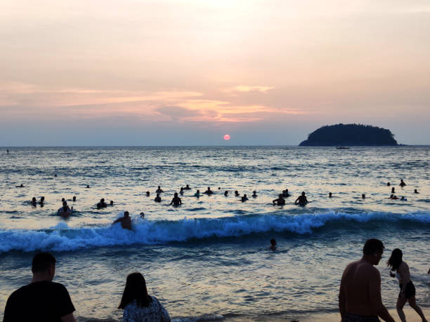 Tourists bathing in the Andaman sea at sunset at Kata Yai Beach, a famous beach in Phuket, Thailand