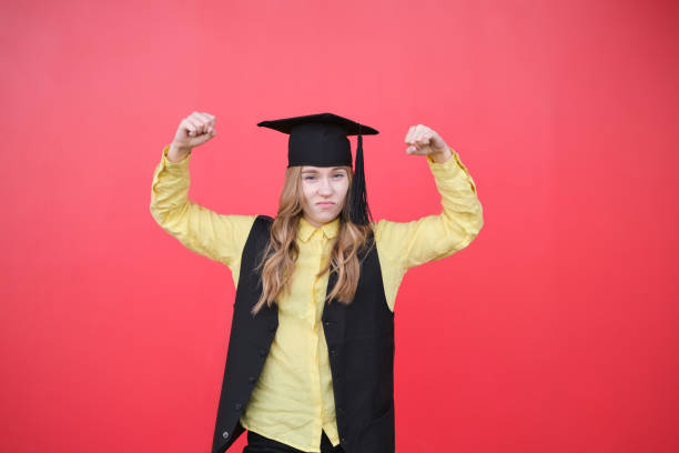 Young beautiful blond female in graduation cap with emotional facial expression on red background. Happy to finish school, college or university High quality photo