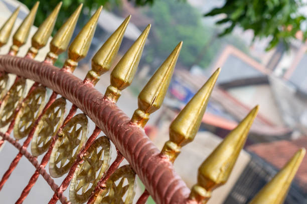 A close-up view of a decorative fence featuring golden spikes and intricate circular patterns. The blurred background highlights the detailed craftsmanship of the fence, providing a contrast between the foreground and the scenery beyond.