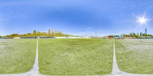 A panoramic view of an expansive artificial turf soccer field bathed in sunlight, embraced by urban facilities and a signature lighthouse in the backdrop. A clear day perfect for sports and recreation