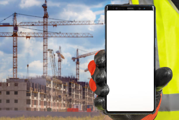 istock Construction apps. Mobile phone in builders hand. Apps for assistance builders concept. Smart phone in front of multi-storey building under construction. Construction of residential buildings 2157671412