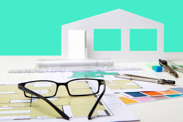 istock Architectural design concept. Architectural drawings next to glasses and a model of house. Architect's desktop close-up. Architectural design services. Creation of apartment-by-room plans. 2157671427
