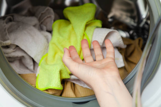 Hands putting dirty laundry in a front-loading washing machine. Close-up