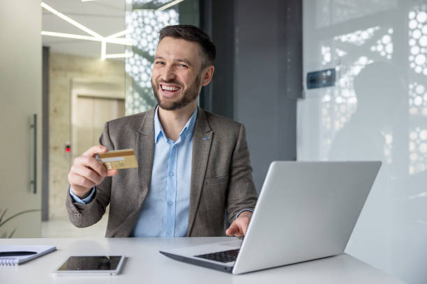 istock Happy businessman holding credit card while working on laptop in office 2157674005