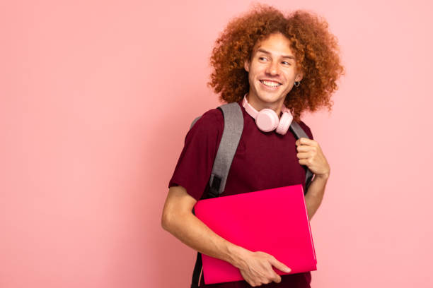 istock Happy student holding books and smiling while looking away against pink background 2157681886