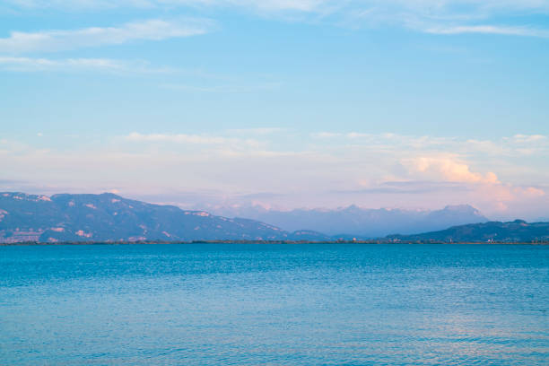 Germany, Beautiful sunset light shining on alps mountain chain behind water of bodensee in summer with snow covered peaks