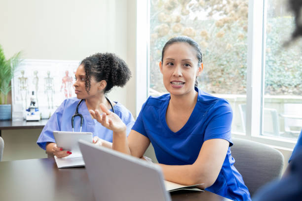 istock In a staff conference setting, a medical professional clad in blue scrubs converses with her colleague. 2157710856