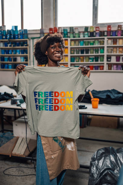 istock Smiling diverse graphic worker showing silkscreen t-shirt at camera 2157711227