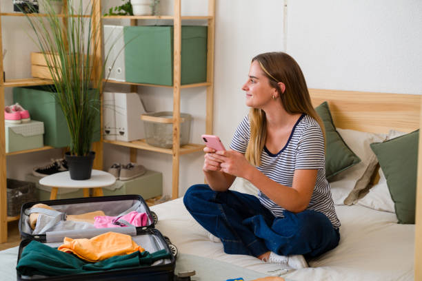 istock Young woman using smartphone while packing a suitcase for travel 2157713275