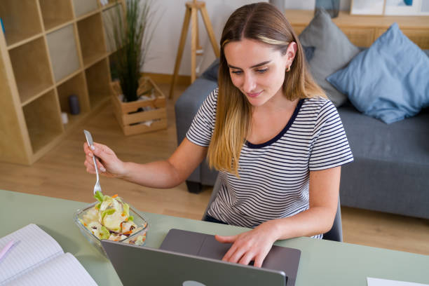 istock Young woman eating salad while working from home office 2157713633