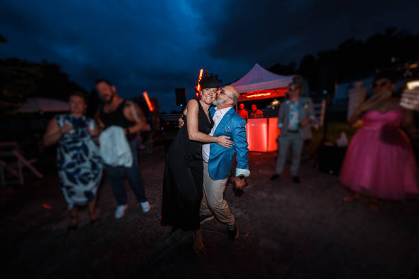 Woman dancing with her partner at wedding reception A woman affectionately embraces her partner and smiles directly at the camera as he gives her a kiss on the cheek, while dancing together at an outdoor wedding reception at night. gay wedding kiss stock pictures, royalty-free photos & images
