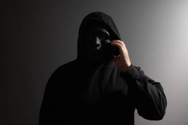 istock Robber, a man in a mask talking on the phone, bandit organizing heist, security threat communicating, masked thief coordinating burglary. 2157717231