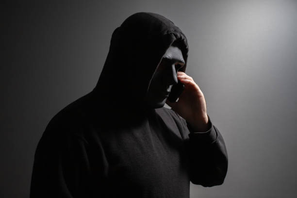 istock A man in a mask talking on the phone, criminal plotting fraud, anonymous hacker preparing cyber attack, burglar coordinating theft. 2157717232