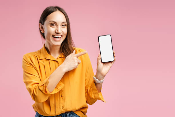 istock Smiling young excited woman holding mobile phone, pointing finger at blank, white screen 2157718655