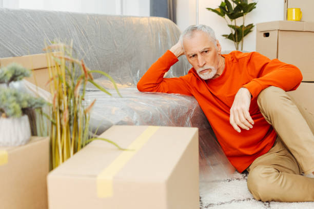 istock Tired senior man sitting on floor feeling sad preparing unpacking cardboard boxes 2157719170