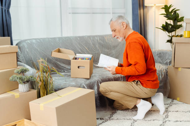 istock Senior man examining belongings while unpacking cupboard boxes at new apartment 2157719187