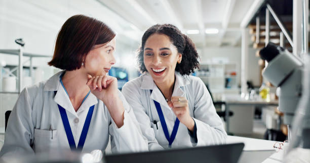 Women, celebration and laptop in lab for science, notification or approval for research project. People, scientist and lab partner with computer for cheers, excited or results for funding application