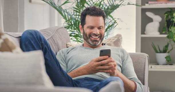 istock Internet meme, phone and relax with man on sofa for social media, laughing and text message. Happy, smile and technology with guy in living room at home for funny joke, connection or digital app 2157720597