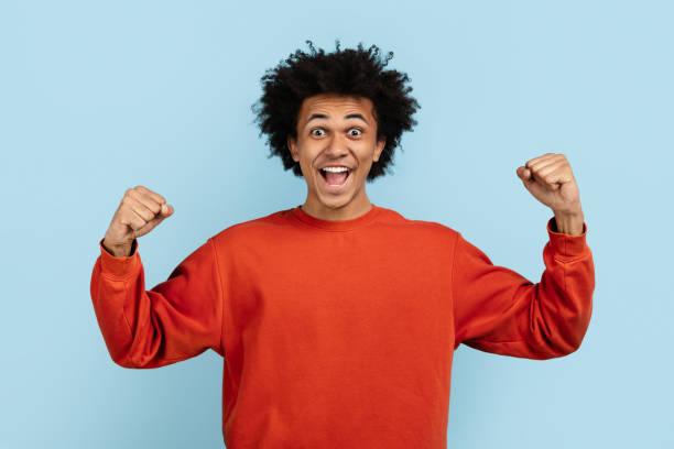 istock Black man celebrating with fists up on blue background 2157720949