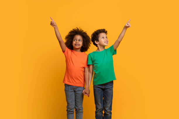 istock Two Young Boys Pointing Upwards Against a Warm Yellow Background 2157722627