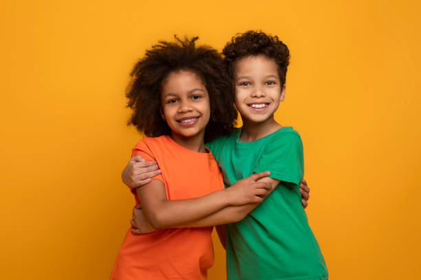 istock Two Children Hugging in Front of Yellow Background 2157722631