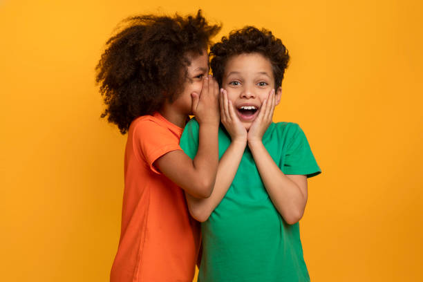 Two Joyful Children Sharing Secrets Against a Bright Yellow Background