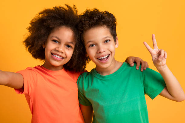 istock Smiling Children Taking Selfie Together Against a Bright Yellow Background 2157723211
