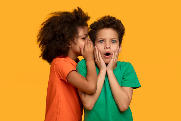istock Two Children Whispering in Front of Orange Background 2157723218
