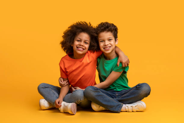 istock Two Children Sitting on a Yellow Background 2157723241