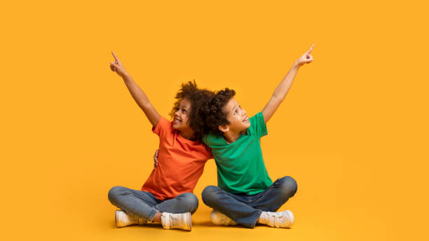 istock Two Children Sitting on Floor Pointing at Something Aside 2157723242