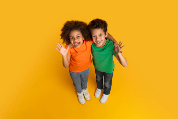 istock Enthusiastic kids waving at camera on yellow background 2157723304