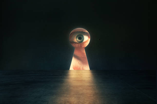Human eye looking through keyhole in concrete wall in dark room