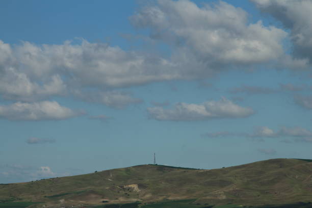 A hill with a tower in the distance. Sky. Outdoor. Nature. Clouds. Promontory
