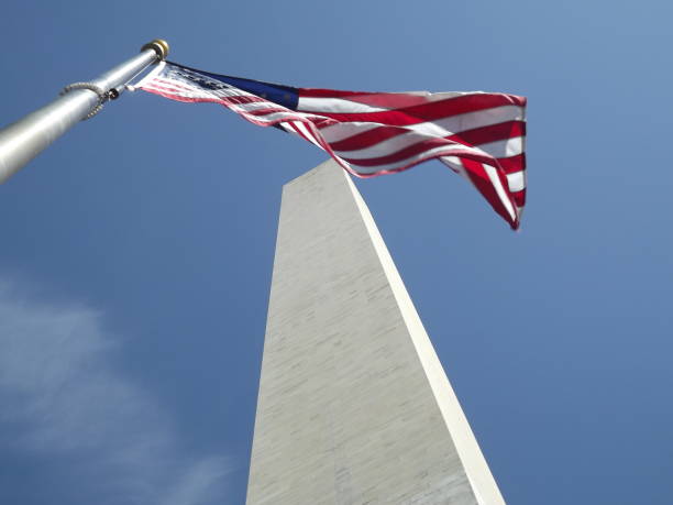 An American flag covers the tip of the Washington Monument in Washington DC. George Washington was the first President of the US and he was a leader in the Revolutionary War.