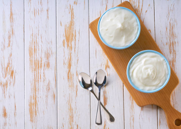 istock Greek yogurt or sour-cream in a blue ceramic bowl on a white table, top view. 2157729225