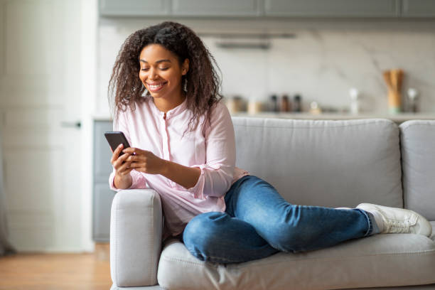 istock Smiling woman using smartphone on couch at home 2157730002