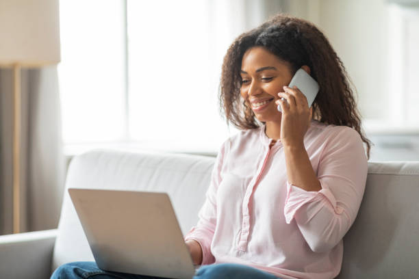 istock Smiling lady on phone with laptop at home 2157730051
