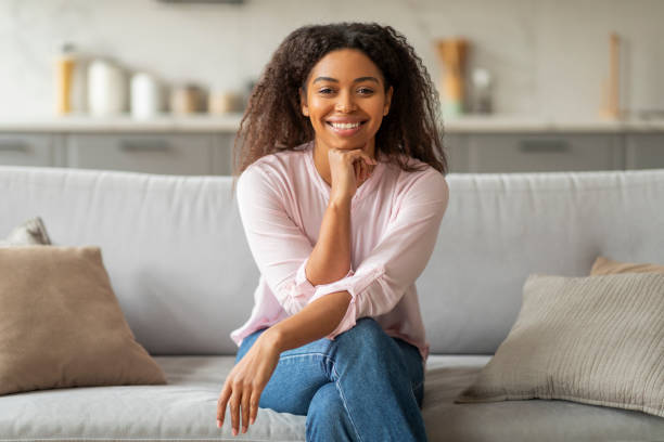 istock Smiling black lady seated on a sofa at home 2157730155