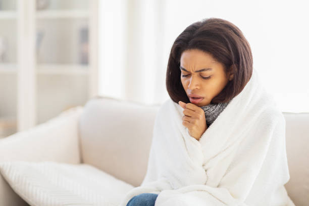 istock Woman Wrapped in Blanket Sitting on Couch, Coughing 2157730358