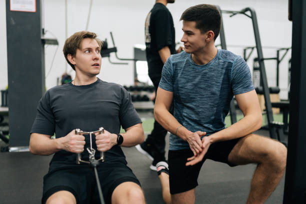 istock Beginner sportsman hard time practicing on rowing machine during sports training with personal coach in health club. Male athlete doing exercise with strap on rowing machine 2157731949