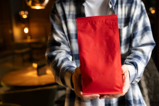 Person Showcasing a Red Coffee Bean Pouch  Package in a Coffee Shop, template copy space