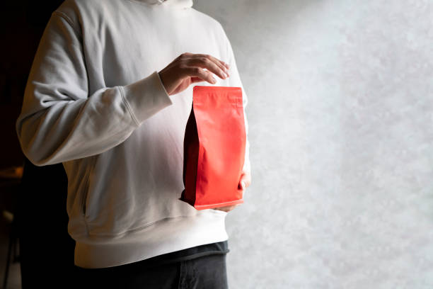 Person Showcasing a Red Coffee Bean Pouch  Package in a Coffee Shop, template copy space