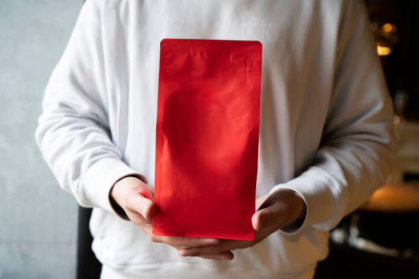 istock Person Showcasing a Red Coffee Bean Pouch  Package in a Coffee Shop, template copy space 2157739961