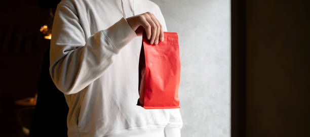 Person Showcasing a Red Coffee Bean Pouch  Package in a Coffee Shop, template copy space