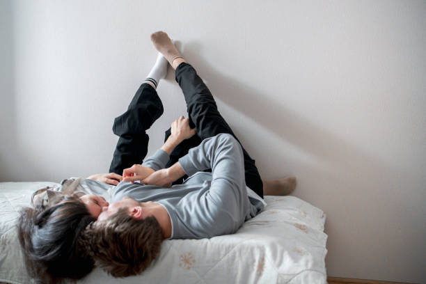 istock A young couple enjoys a relaxed, affectionate moment together while lying on a bed, with their legs playfully extended upwards against a white wall. 2157740162